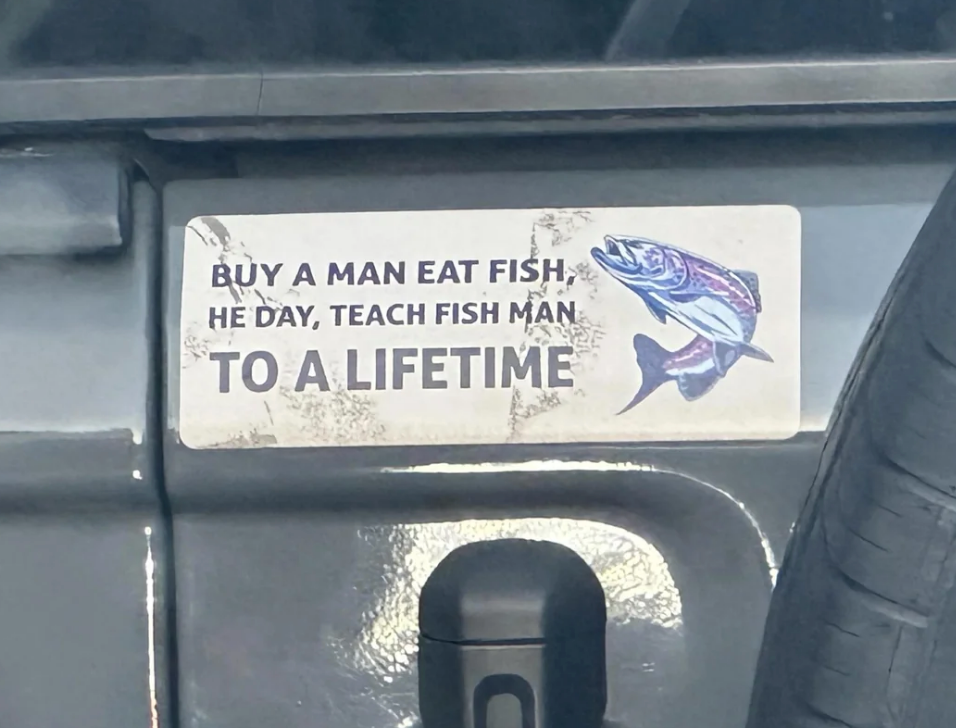 Bumper sticker with a fish illustration that appears to read: "Buy a man eat fish he day, teach fish man to a lifetime"