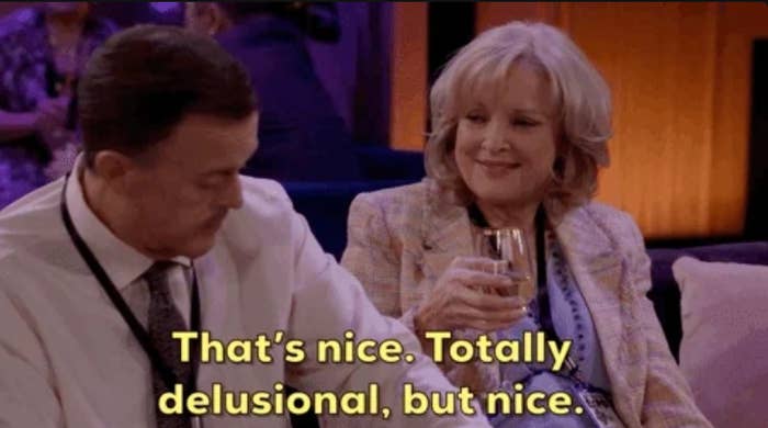 Two people sitting on a couch; one holds a drink and smiles. Subtitle: "That's nice. Totally delusional, but nice."