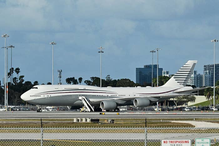 A large passenger airplane is parked on an airport runway with city buildings visible in the background