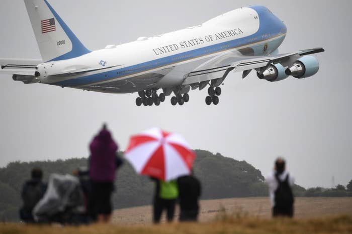 Air Force One takes off, with onlookers holding umbrellas in the foreground