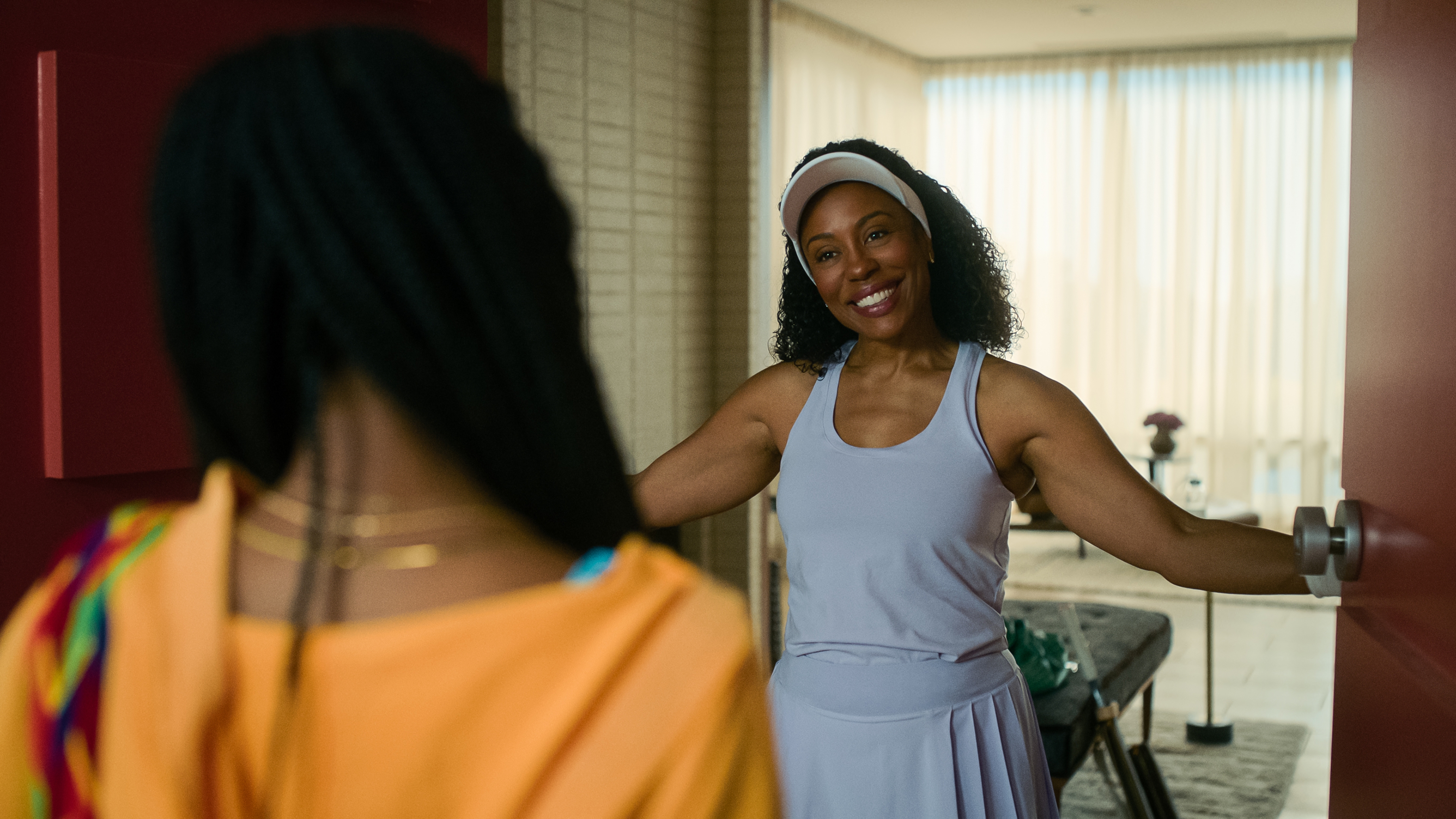 Person in athletic wear smiling warmly at a visitor standing in a doorway
