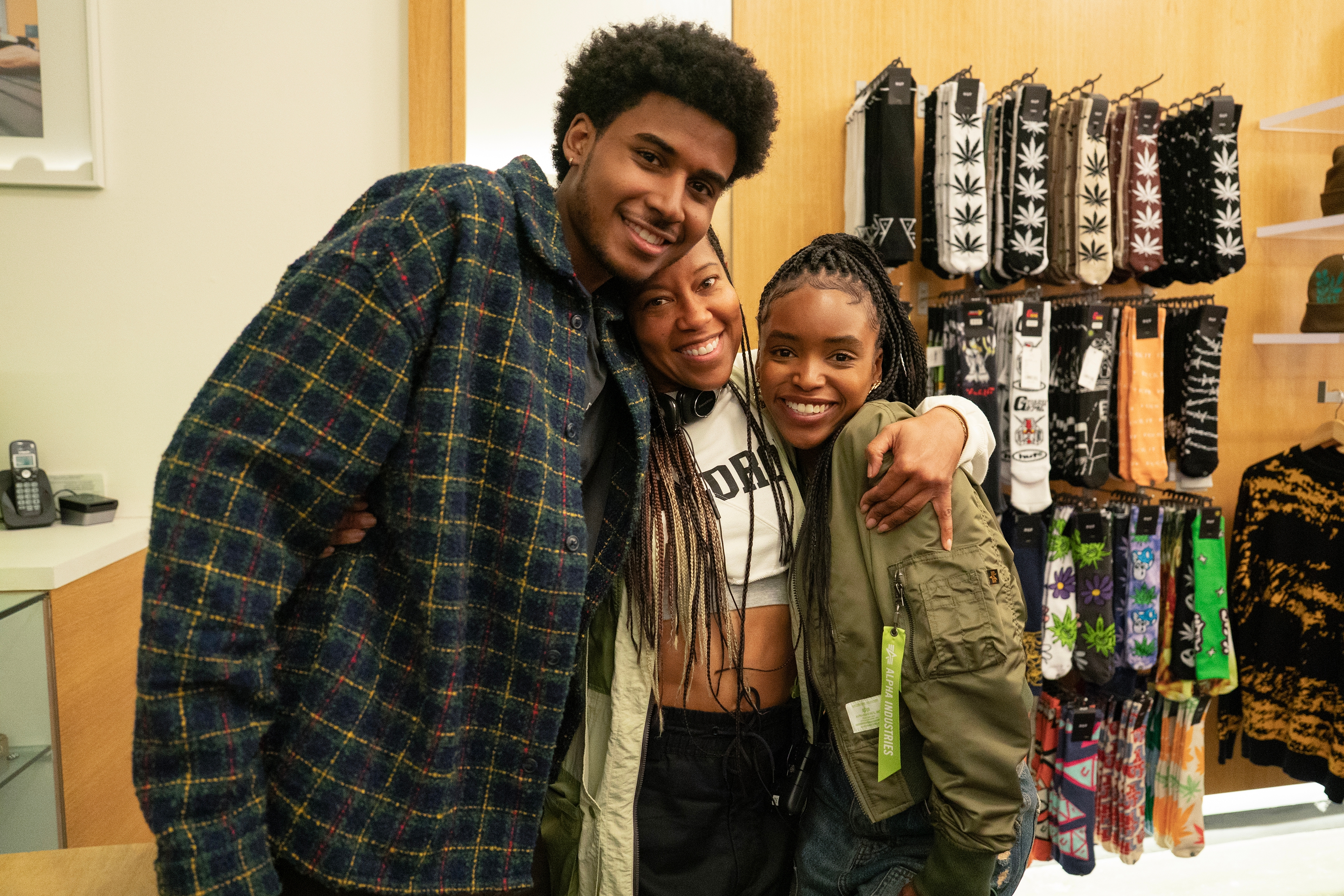 Three people smiling and hugging in a store. They are standing in front of shelves displaying various patterned socks. Casual and cozy styling
