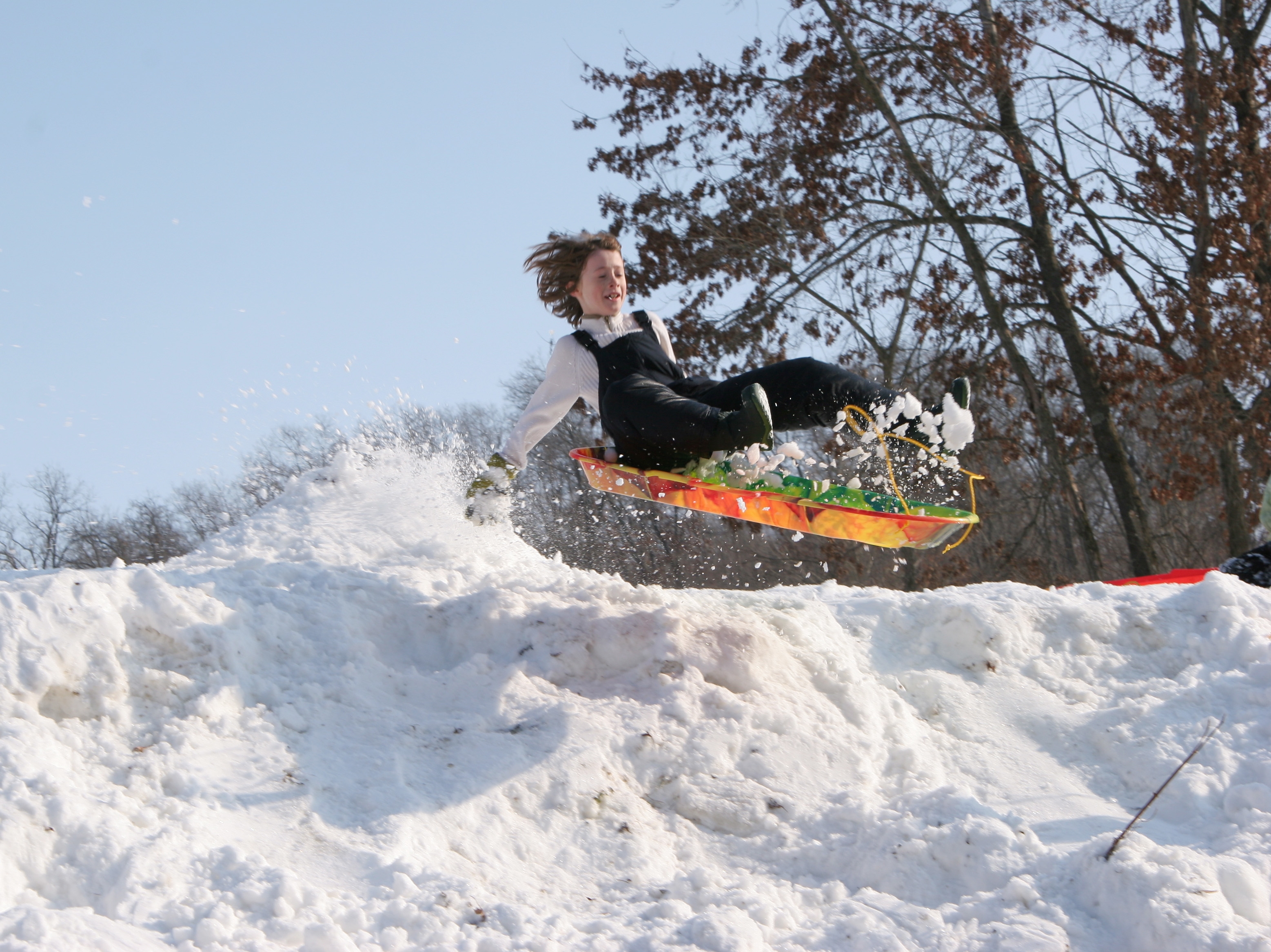 Person joyfully sledding down a snowy hill, mid-air, wearing a winter coat and boots