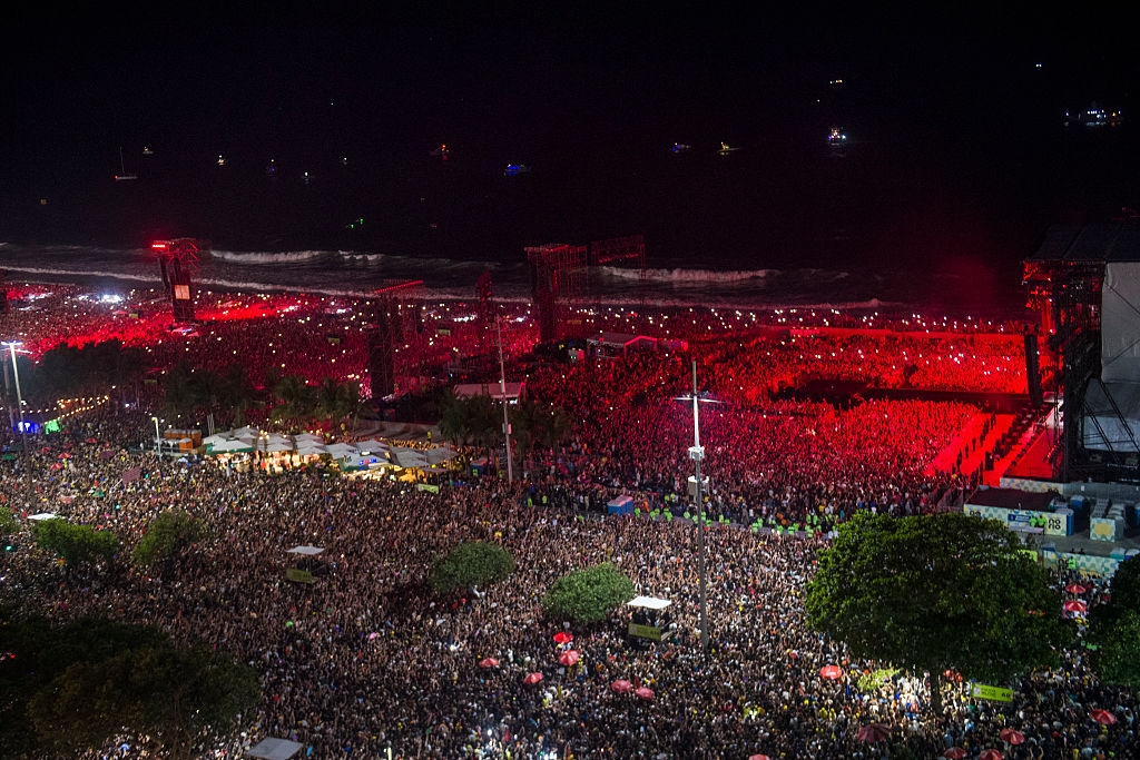 Aerial view of a massive outdoor concert at night, with a dense crowd and stage lights illuminating the scene