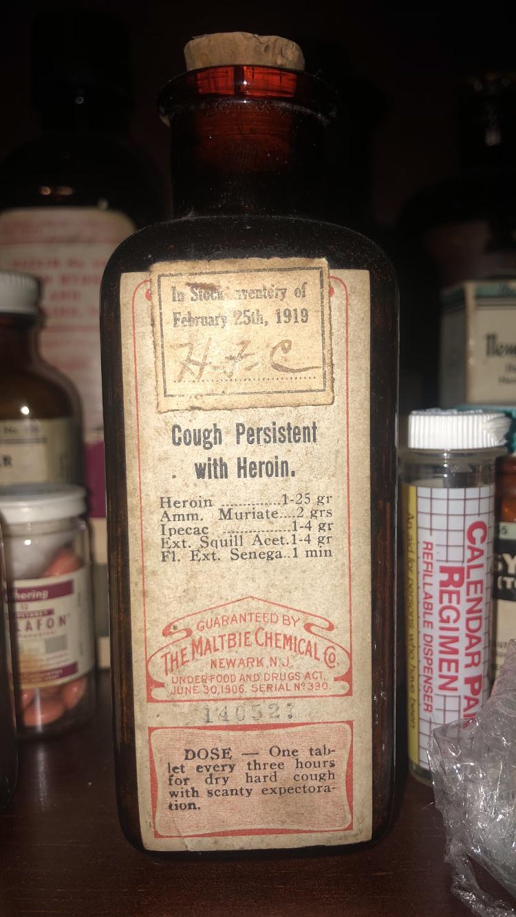 Vintage bottle labeled "Cough Persistent with Heroin," dated 1919, lists ingredients including heroin and dosage instructions