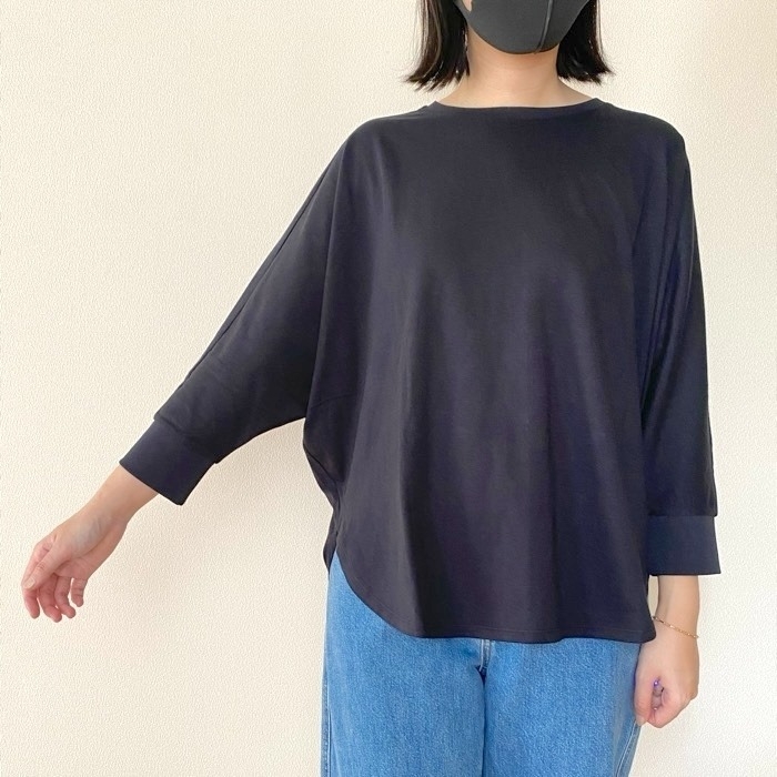 女性がシンプルな長袖シャツとジーンズを着てポーズを取っている。顔はマスクで隠れている。