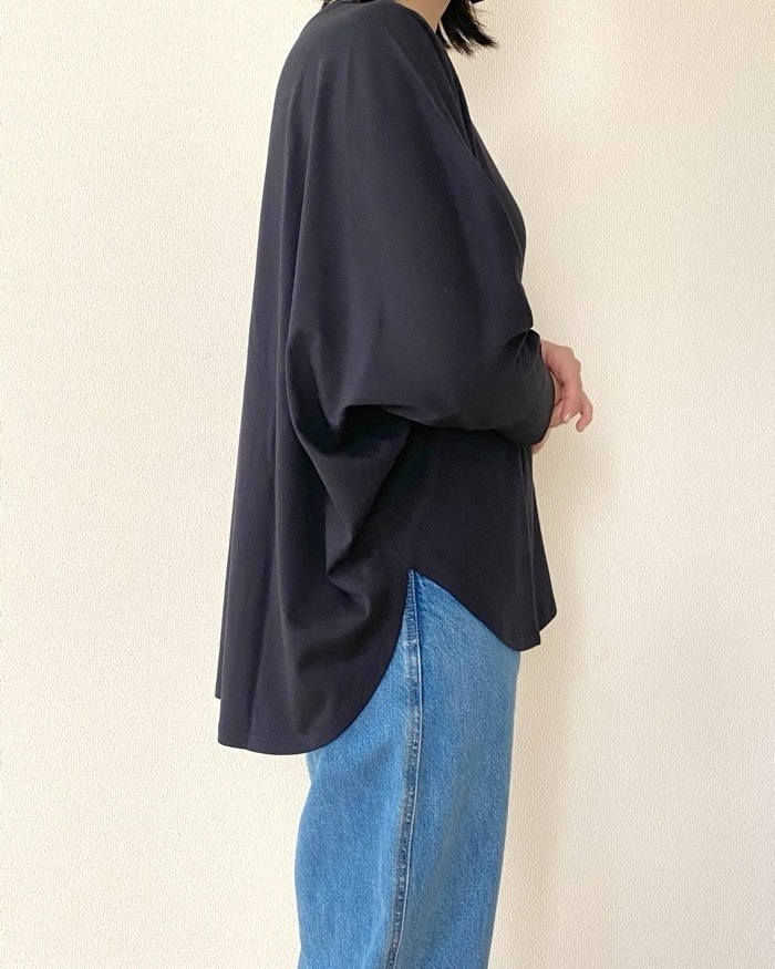 ゆったりした黒のトップスとデニムを着た人物が横を向いている。上品でカジュアルな装い。