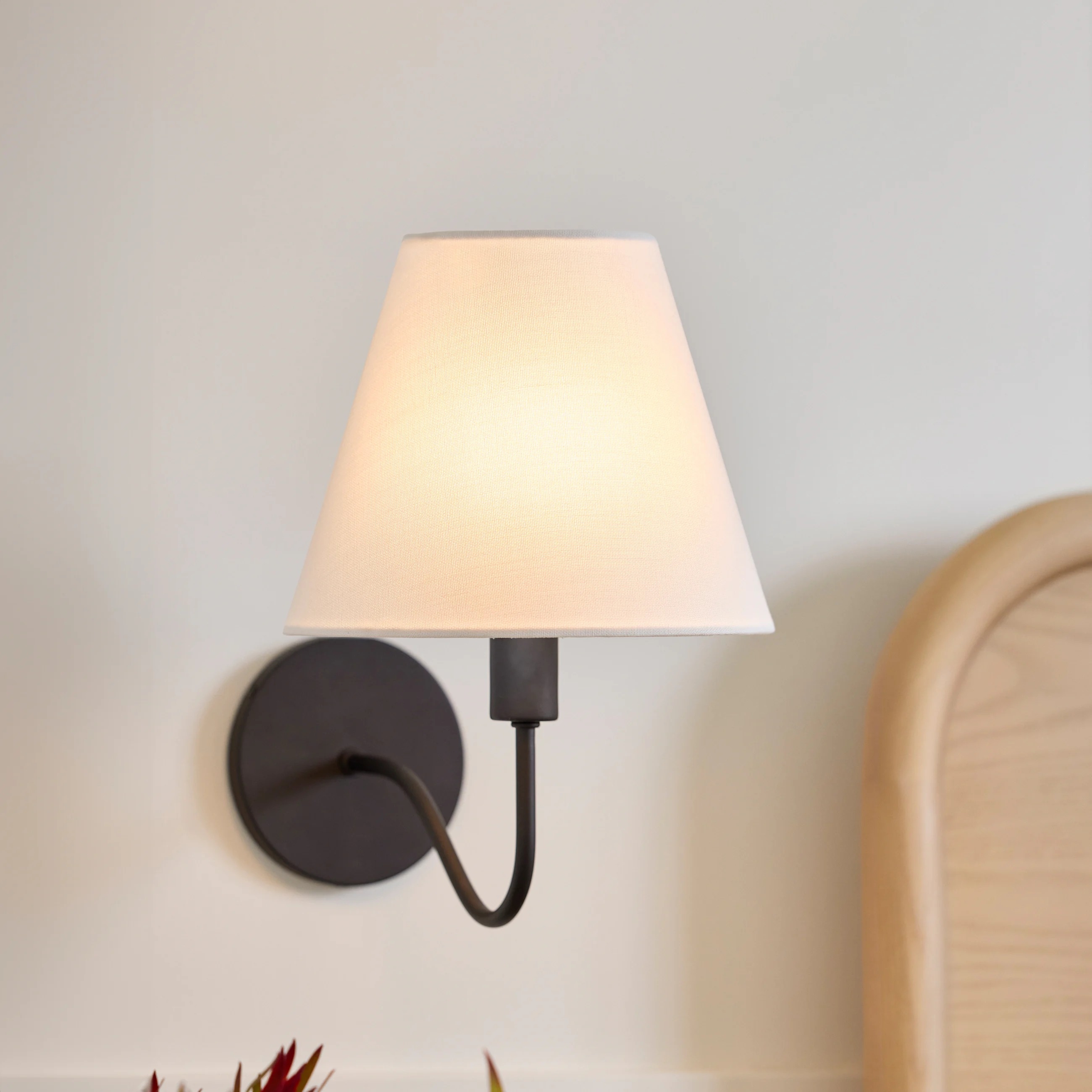 Elegant wall-mounted lamp with a simple fabric shade, illuminating a cozy corner beside a wooden headboard. Ideal for bedroom decor
