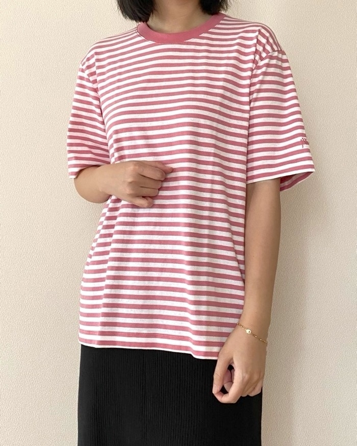 ストライプ柄のTシャツを着た人物が壁の前に立っている。