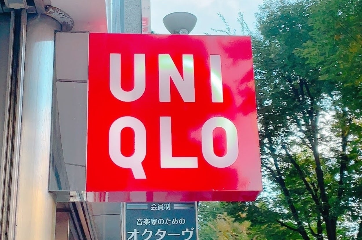ユニクロの店舗看板が店舗外壁に設置されている。背景に木が見える。