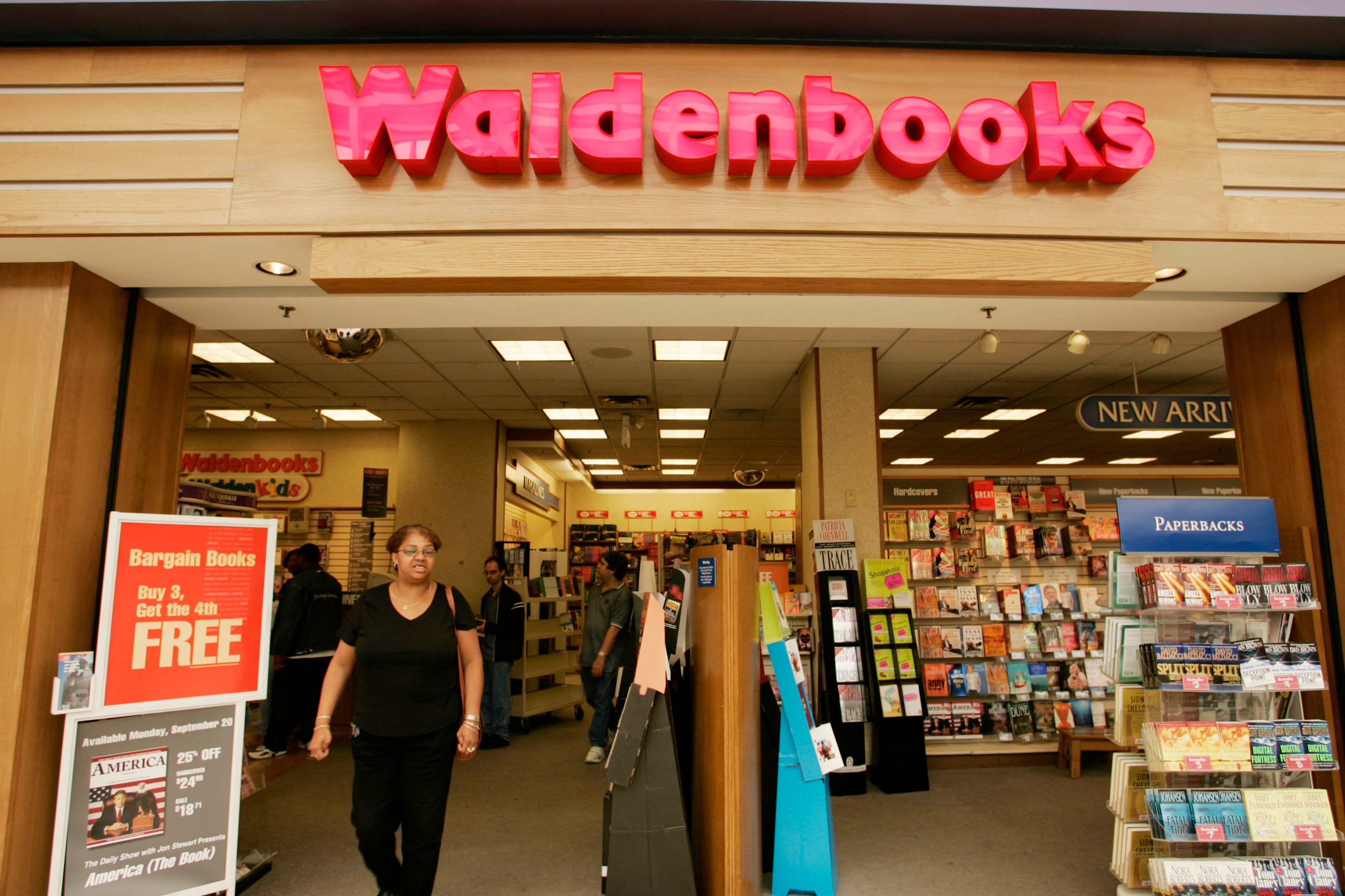 Person exiting a Waldenbooks store filled with books and magazines, with signs advertising bargains and new arrivals