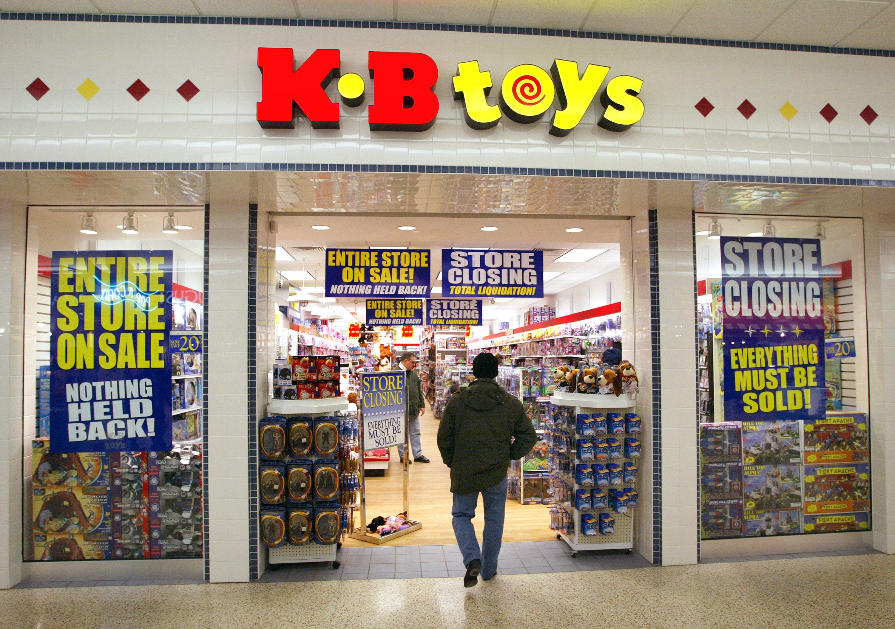 A person enters a KB Toys store with signs stating "Entire Store On Sale" and "Store Closing, Everything Must Be Sold."
