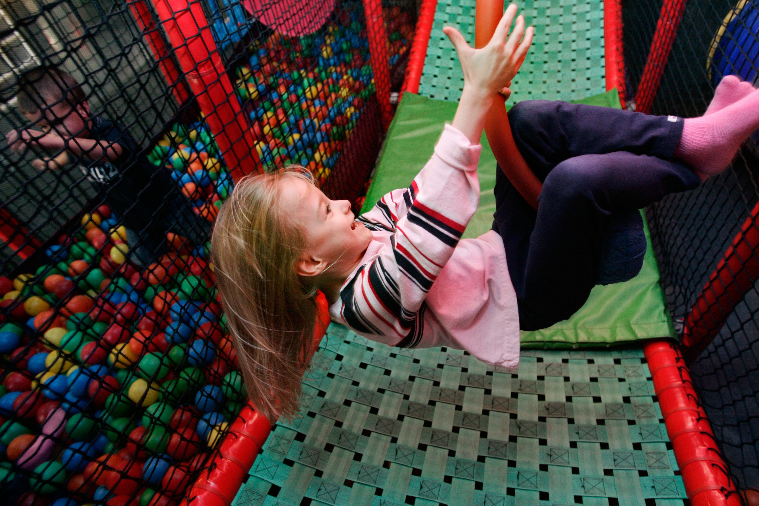 Child swinging on a rope in a play area with colorful balls and netting, smiling and having fun