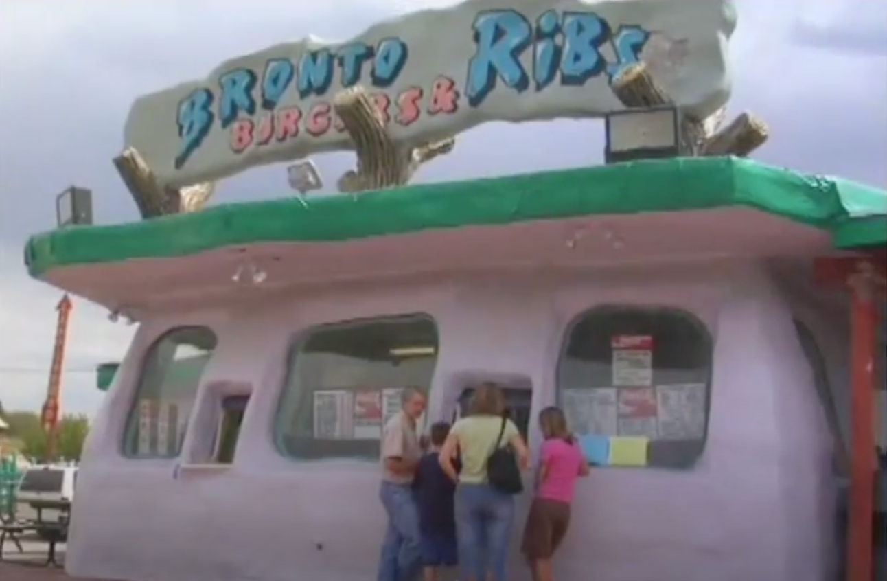People outside a diner with a cartoon-style sign for "Bronto Burgers & Ribs."