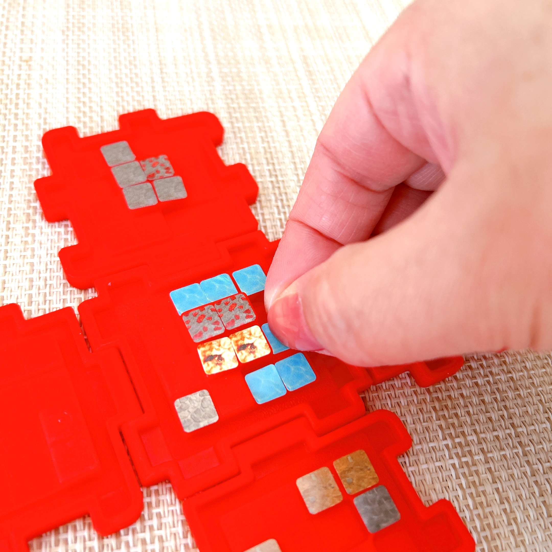 赤いボードにカラフルなタイルを配置する手。