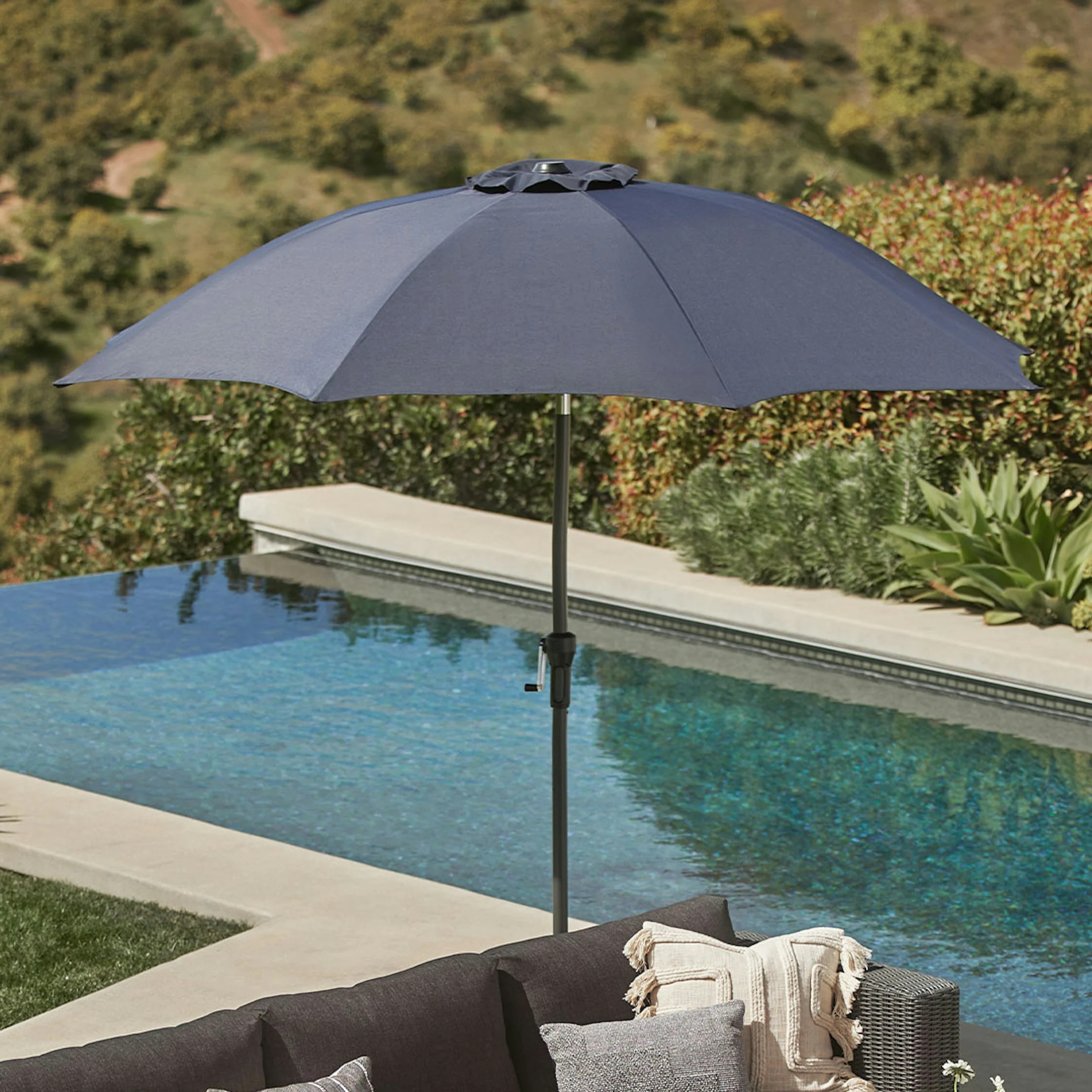 Patio with a large umbrella by a pool, surrounded by greenery, ideal for outdoor leisure