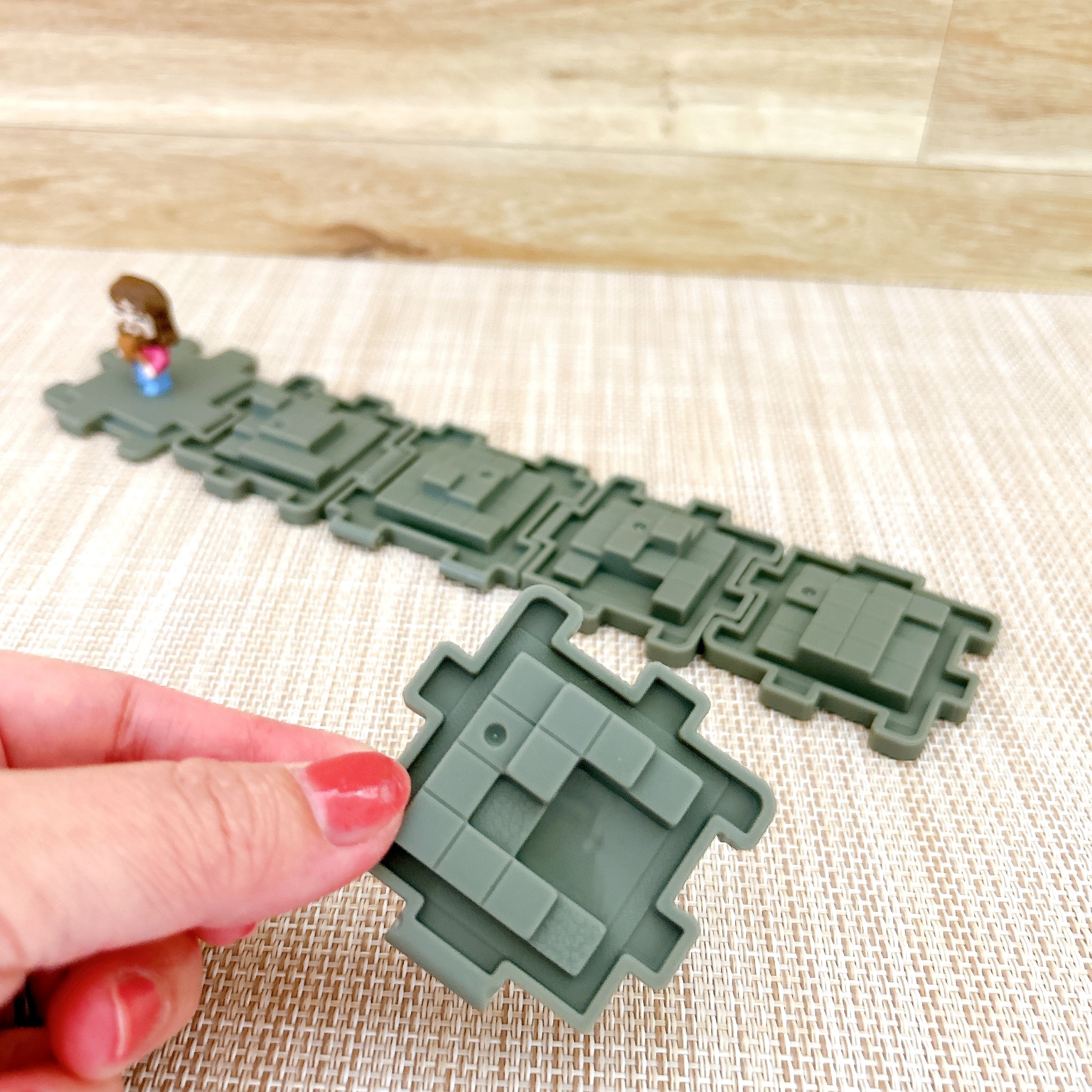 手にしたパズルピースを背景のパズルに組み込もうとしている場面。背景に小さな人形があります。