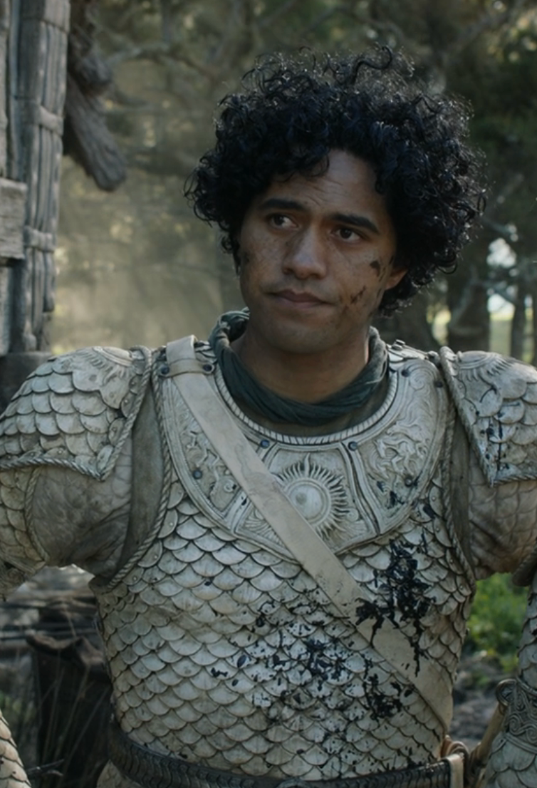 Person in detailed medieval-style armor with a contemplative expression, standing outdoors