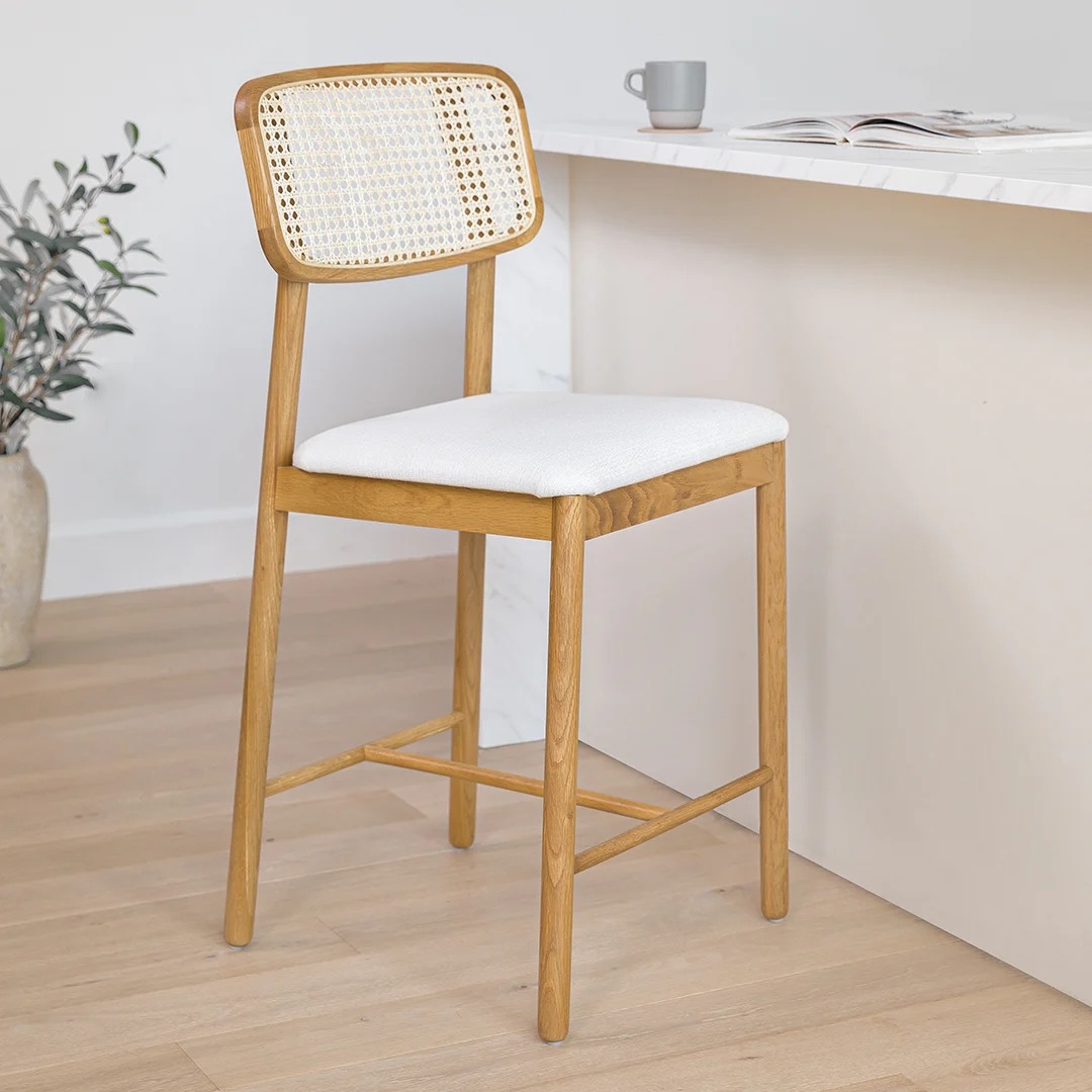 Wooden bar stool with a woven backrest and cushioned seat next to a white countertop, in a minimalist kitchen setting