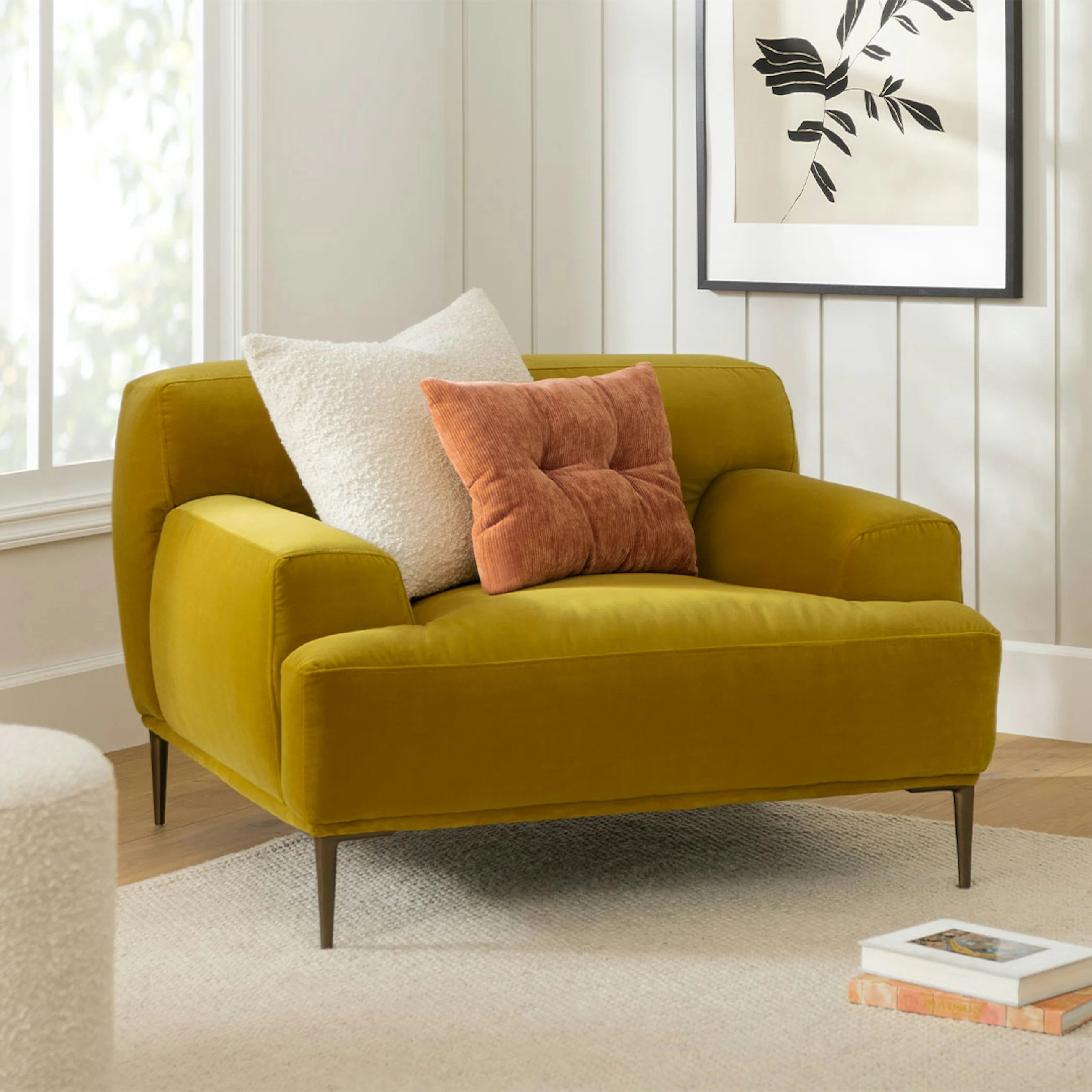 Cozy armchair with a mustard yellow fabric, white and pink throw pillows, and wooden legs, placed in a modern living room setup