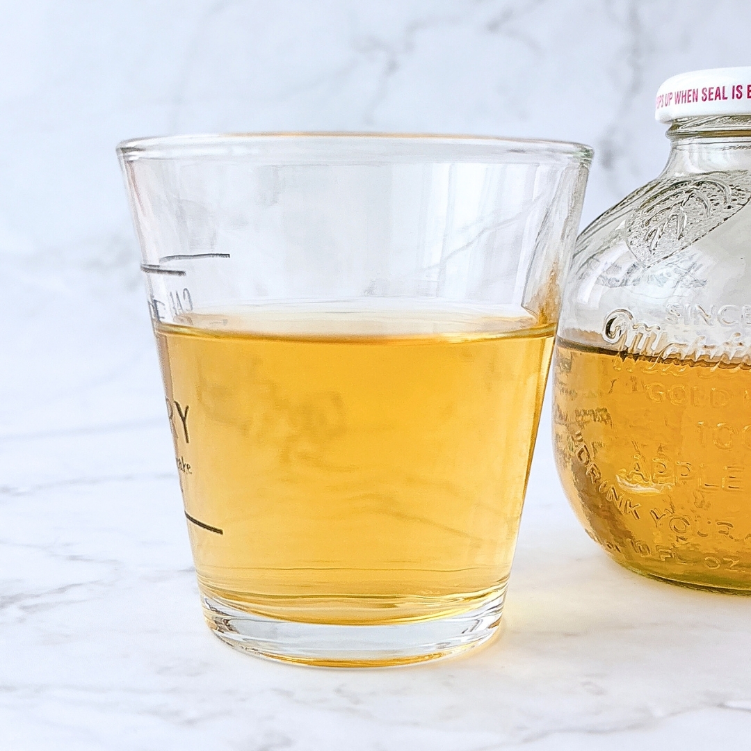 ガラスカップに注がれたリンゴ風味の飲み物と瓶が並んでいる。白い背景。