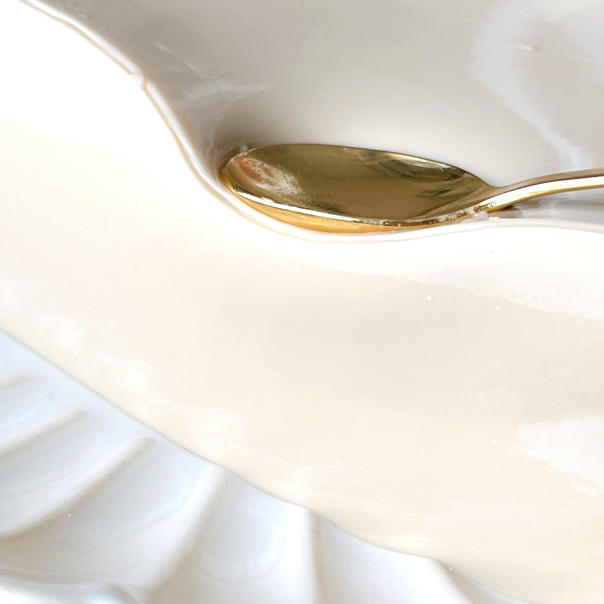 白い陶器の器にゴールドのスプーンが置かれたシンプルな構図。