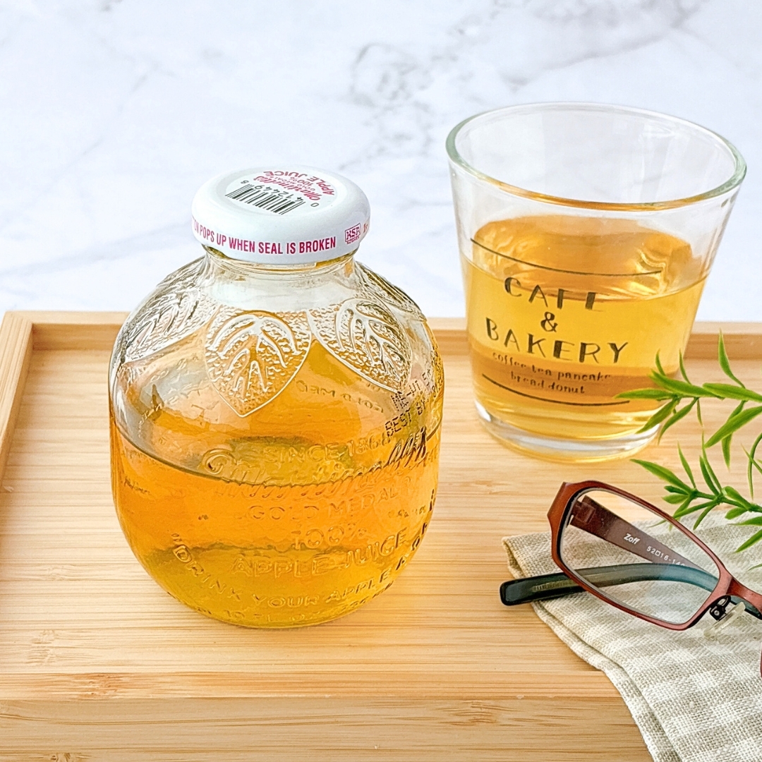 木製トレーに置かれたフルーティーな飲み物の瓶とカフェのグラス。横に眼鏡と布がある。