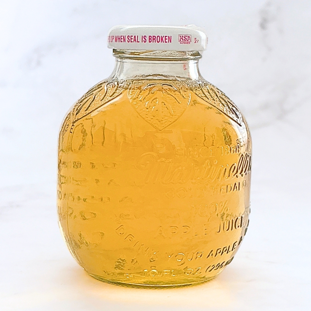 リンゴジュースの瓶、透明なガラスにエンボス加工のデザインと白いキャップ。