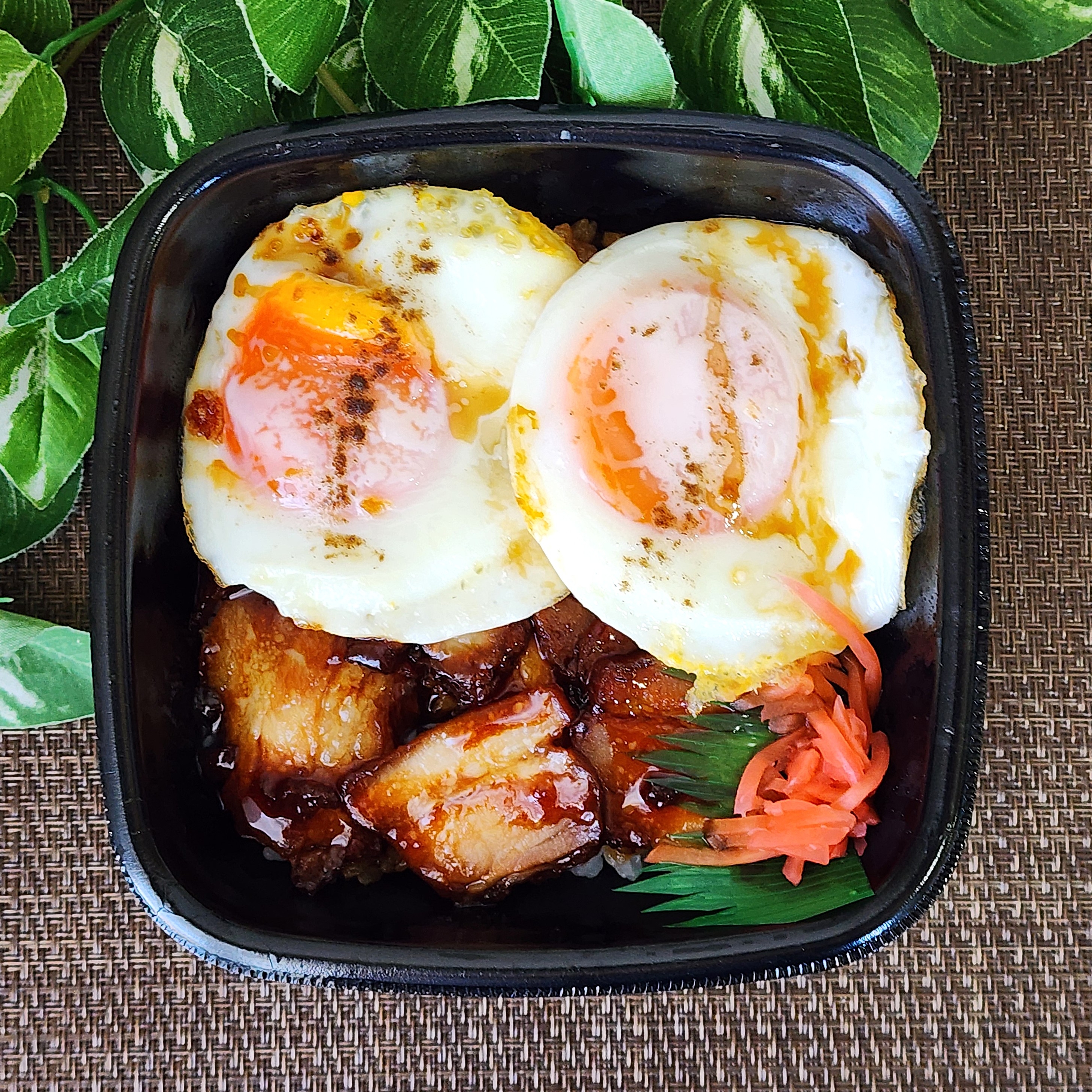 目玉焼きと焼豚がのった弁当。葉の背景添え。