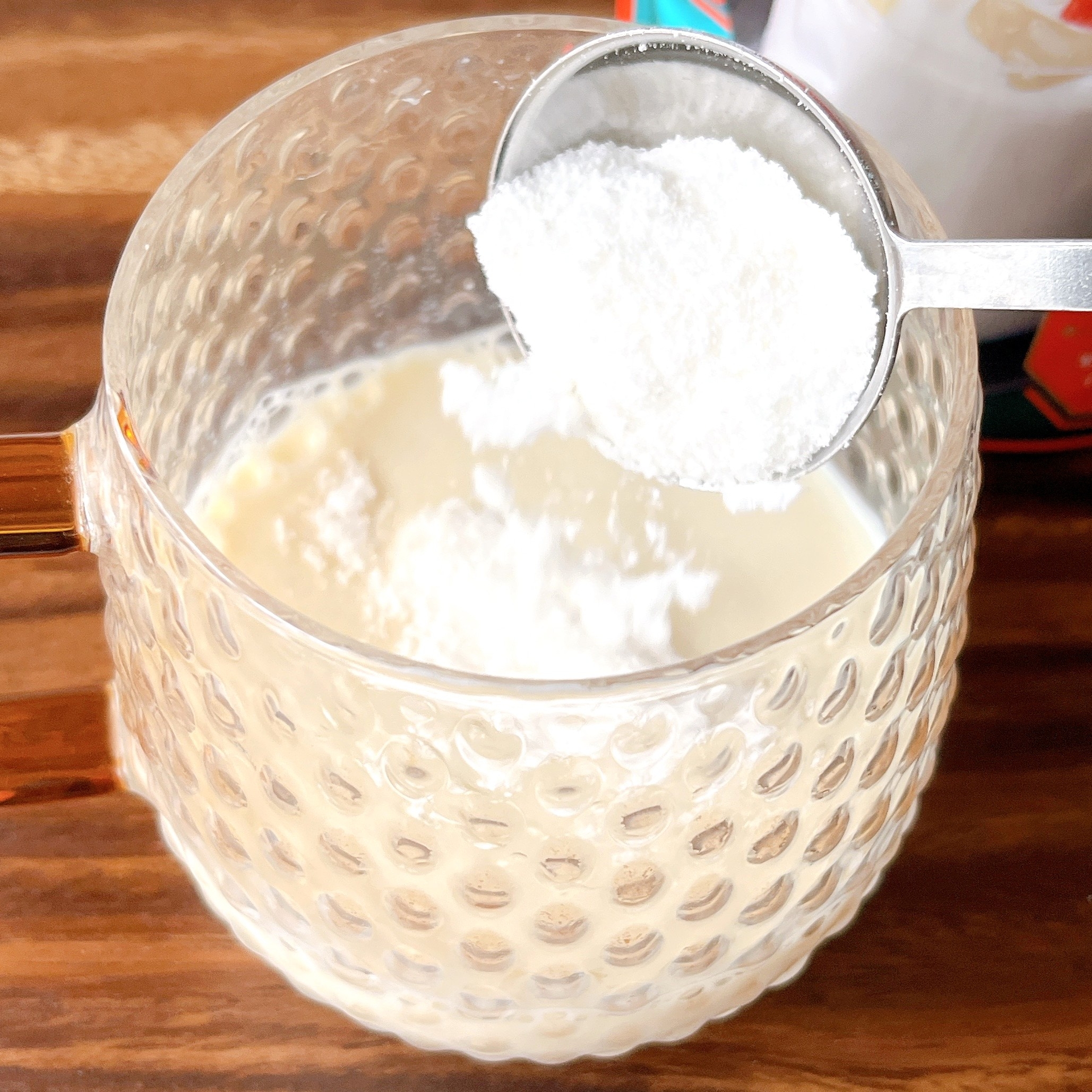 透明なガラスカップに入ったミルクに、スプーンで粉末を加えている様子。