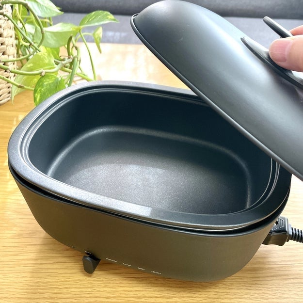 黒い電気コーヒーメーカーの蓋が開いている様子。テーブルの上に配置。