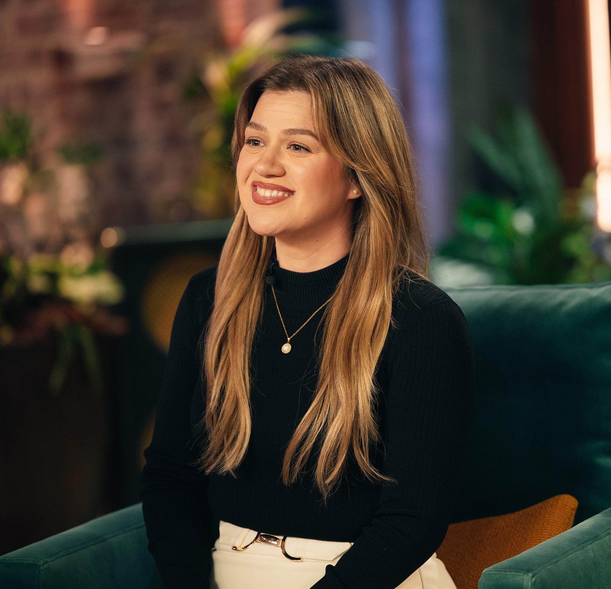 Kelly Clarkson sitting on a green chair, smiling
