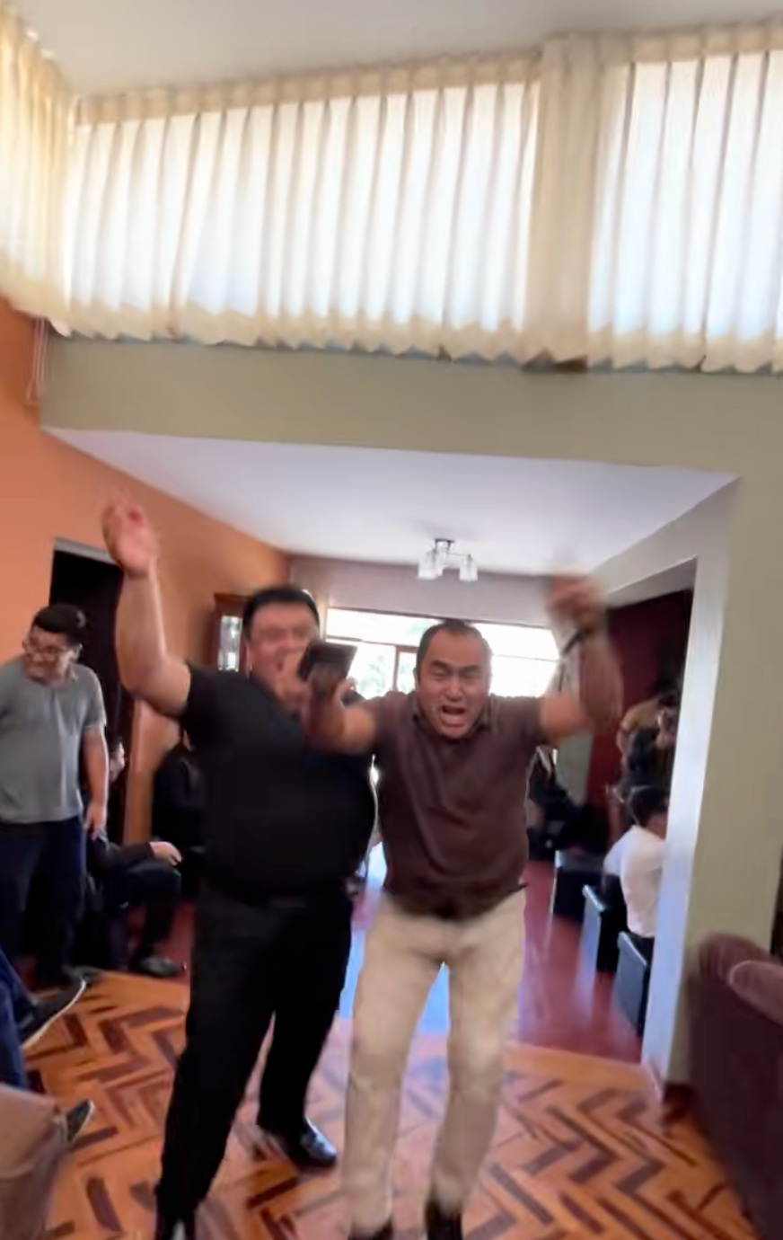 Two people are joyfully celebrating indoors with others in the background
