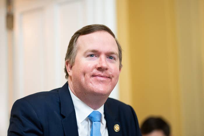 A person in a suit and tie is smiling, appearing to attend a formal or professional event indoors