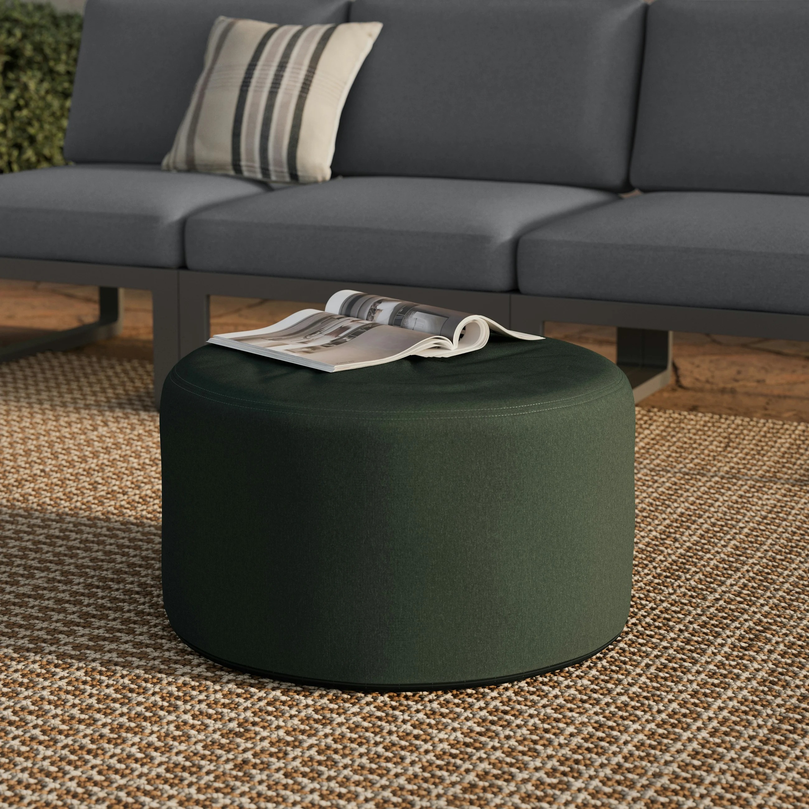 Round ottoman with a magazine on top, set on a patterned rug in front of a gray outdoor couch
