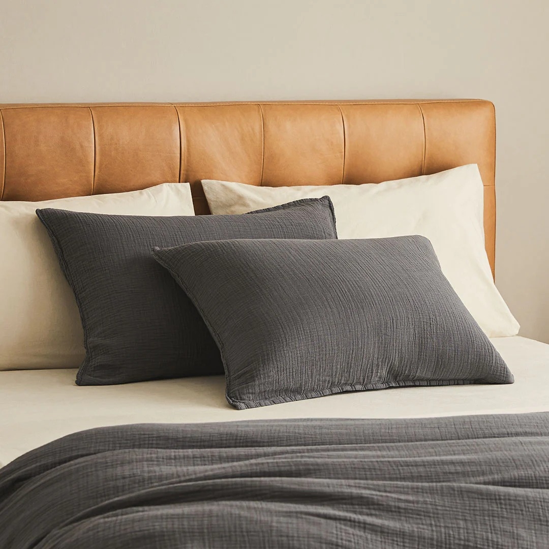 Bed with a tan headboard, dark gray pillows, and matching duvet, showcasing cozy, modern bedroom decor