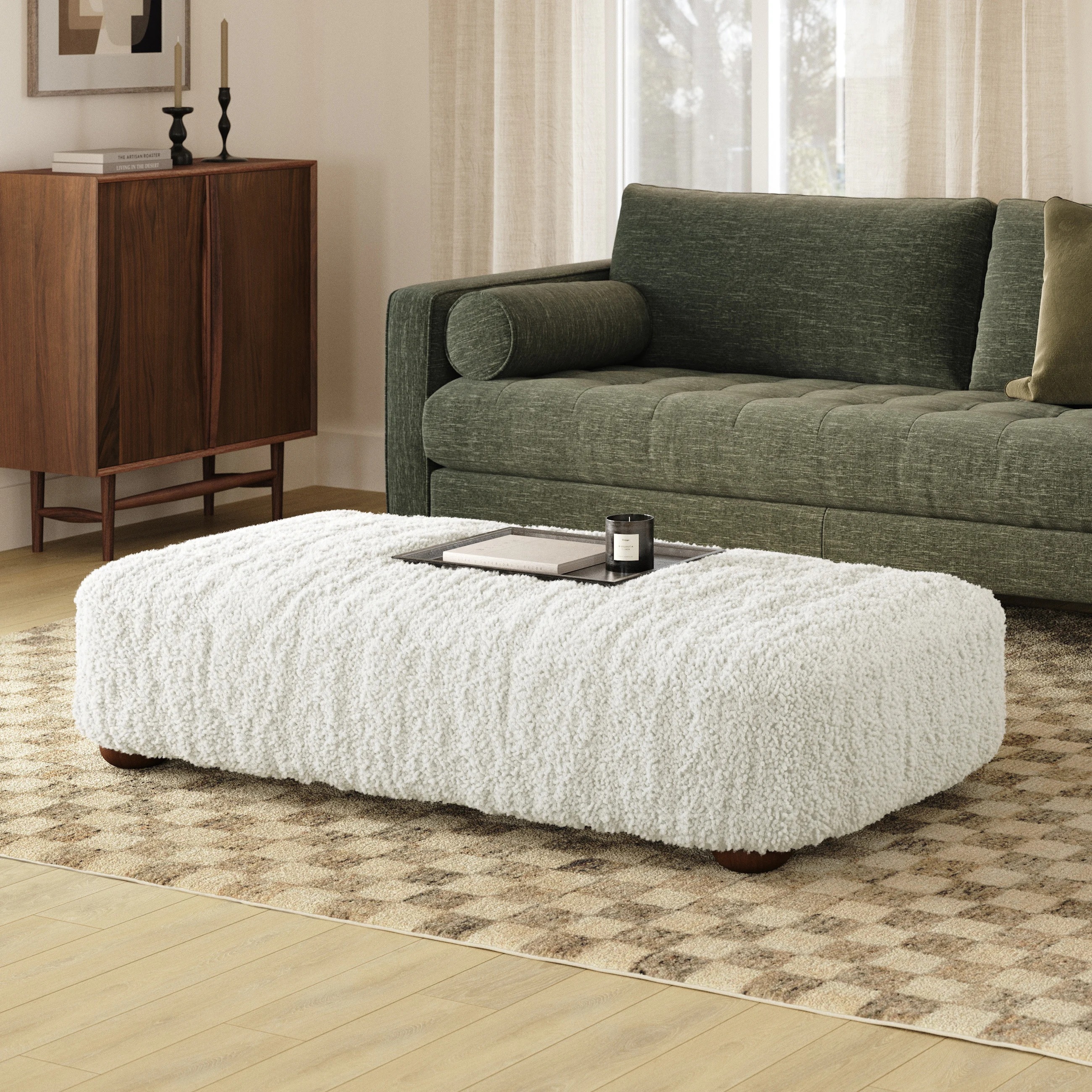 Modern living room with a plush white ottoman, a green sofa, and a wooden cabinet. Neutral decor emphasizes comfort and style
