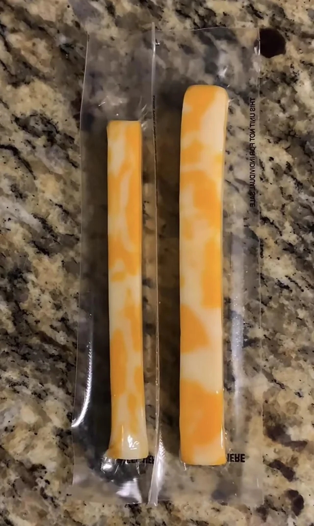 Two packaged cheese sticks lie on a speckled countertop