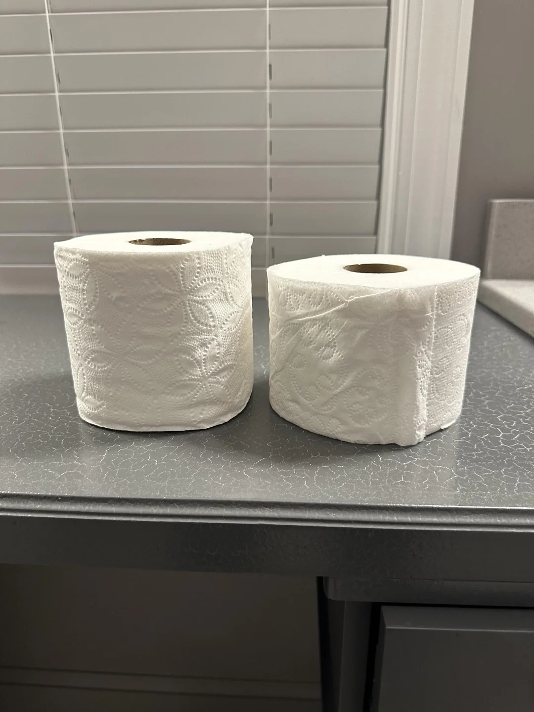 Two toilet paper rolls side by side on a counter, one significantly compressed, illustrating a potential manufacturing or storage issue