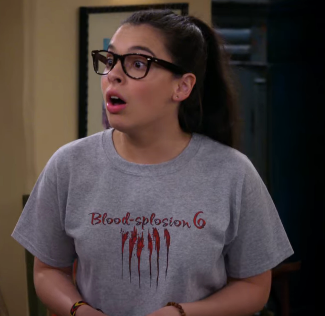 A person with glasses, surprised expression, wearing a "Blood-splosion 6" T-shirt