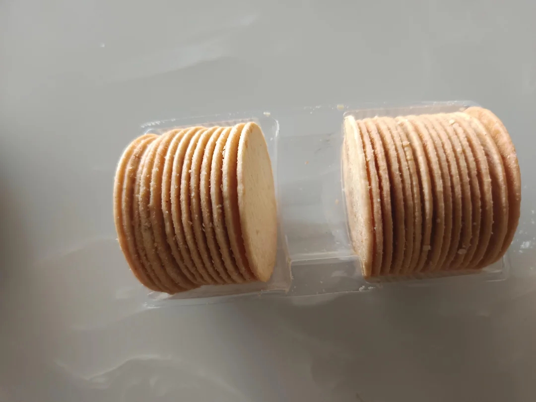 Two stacks of thin, round crackers sit in a plastic container on a flat surface