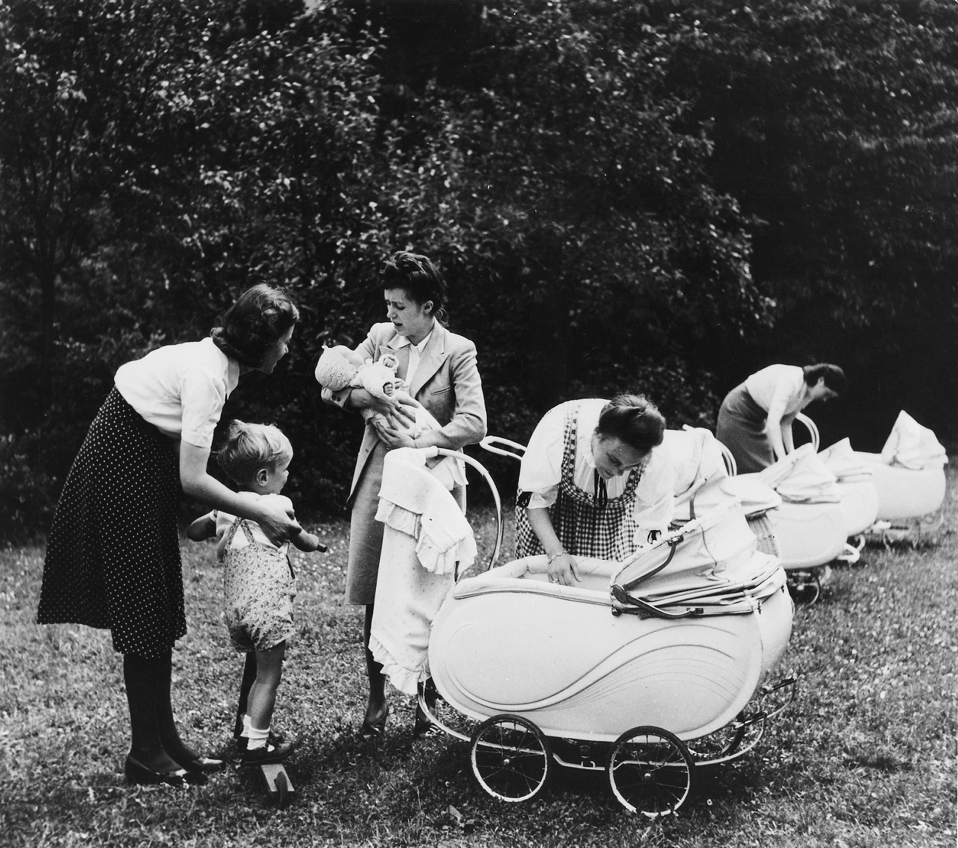 Women with a young child and babies in vintage prams in a park setting, mid-20th century