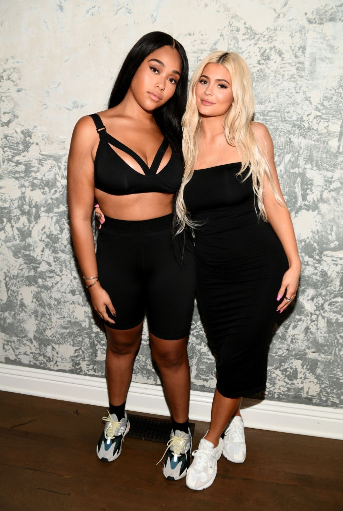 Two women pose together; one in sporty athleisure, the other in a fitted dress and sneakers. They stand close with a casual backdrop
