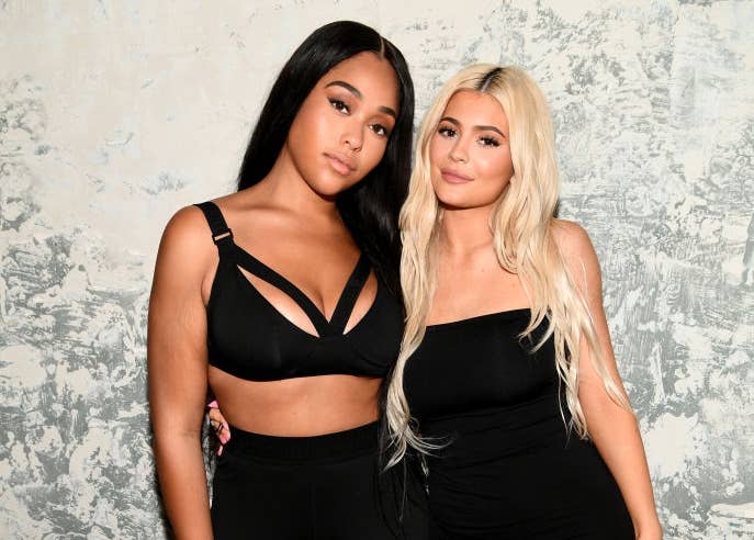 Two women pose together; one in sporty athleisure, the other in a fitted dress and sneakers. They stand close with a casual backdrop