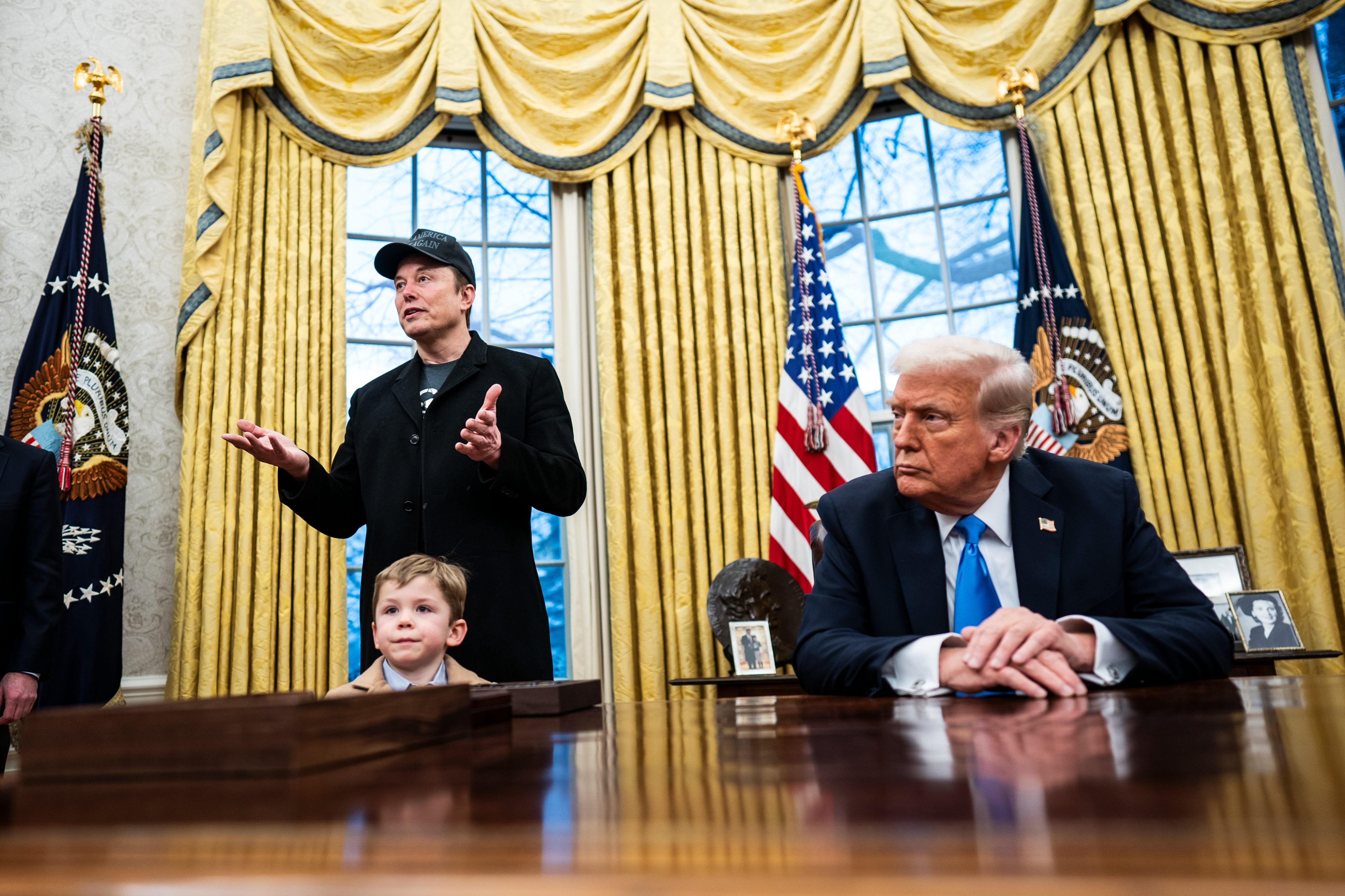 Donald Trump listens as Elon Musk speaks in the Oval Office, standing behind young son X Æ A-Xii