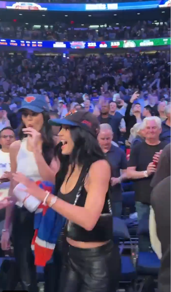 People in a lively crowd at a sports event. The focus is on two women wearing stylish hats and outfits, enjoying the game with enthusiasm