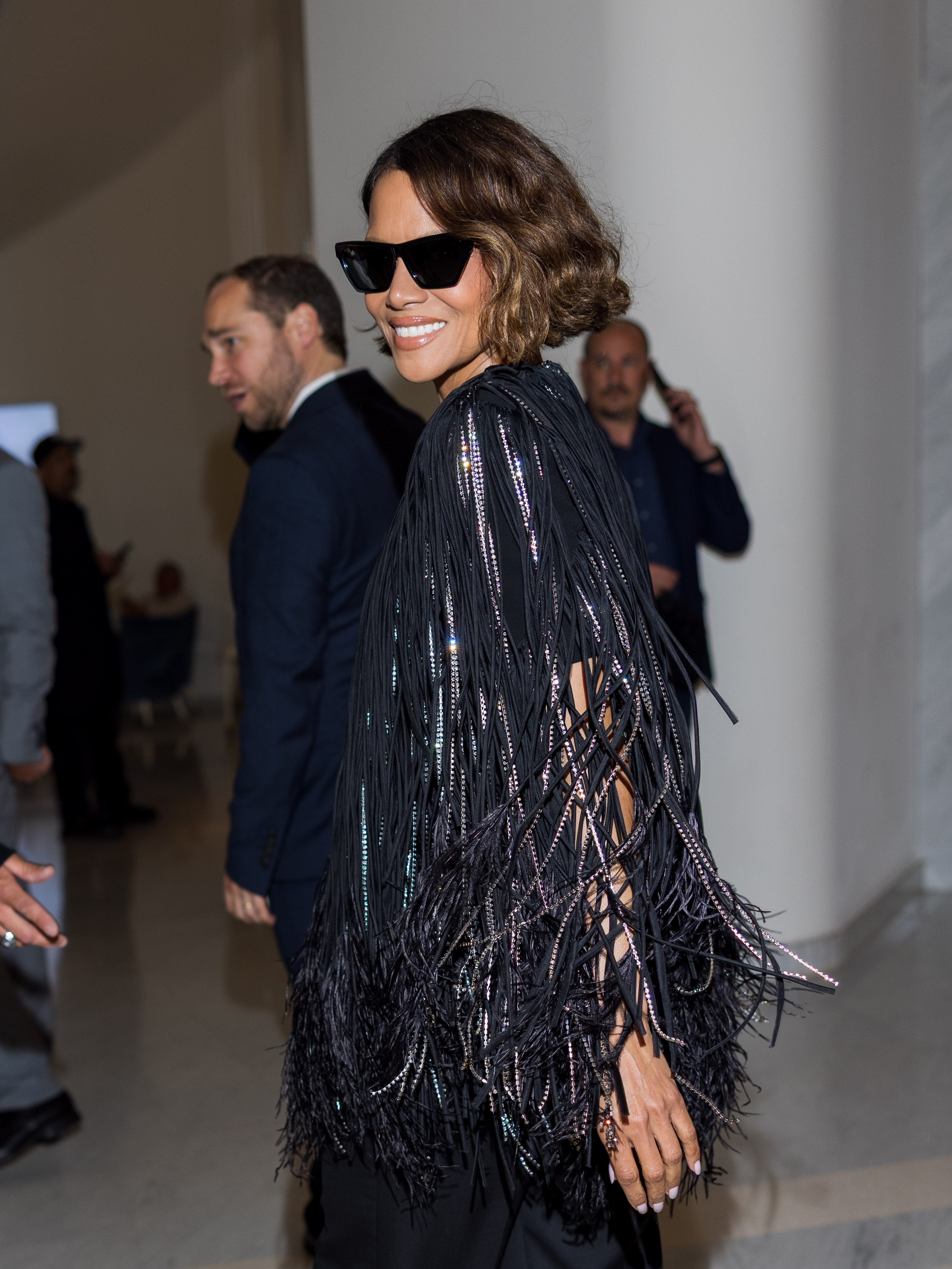 Person in stylish fringed outfit and sunglasses smiling at an event