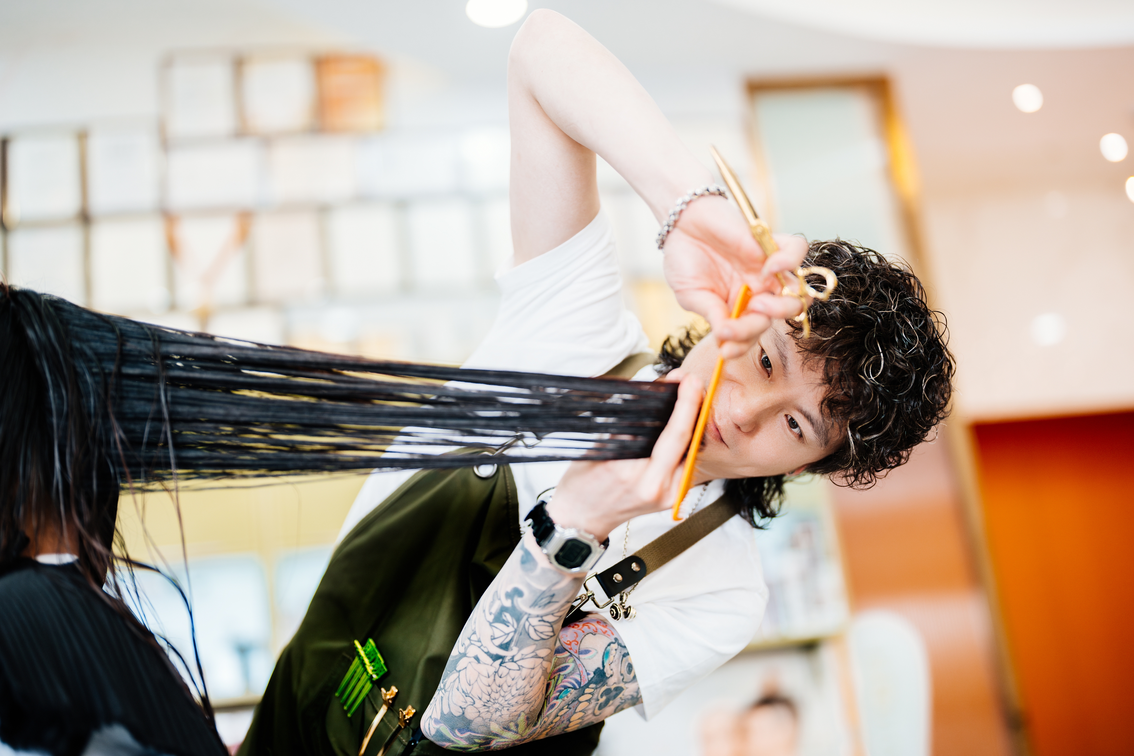 Hairdresser with tattoos precisely cuts long, wet hair in a salon, using scissors and comb