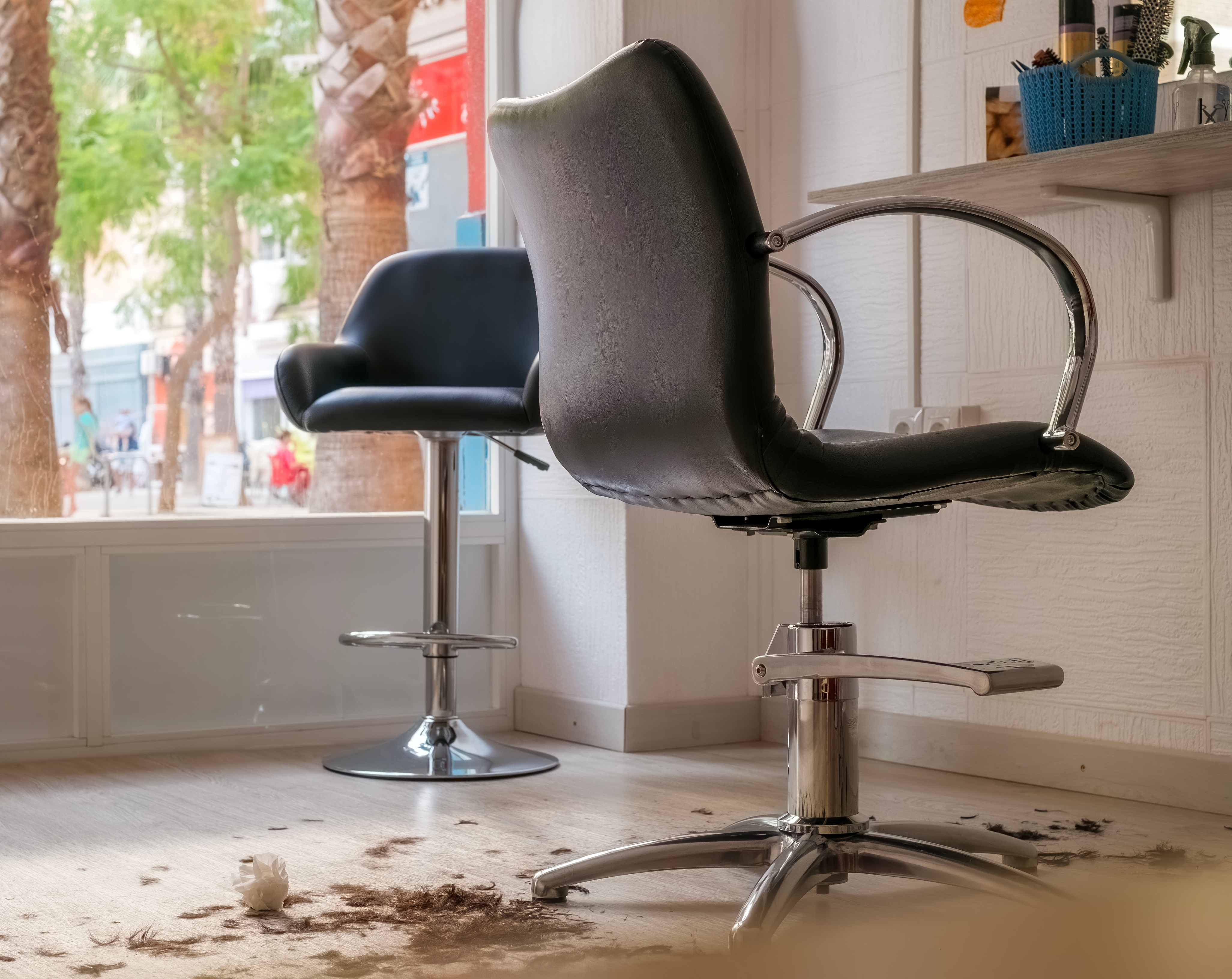 Empty salon chairs near a shelf with hair clippings on the floor, suggesting a recently completed haircut