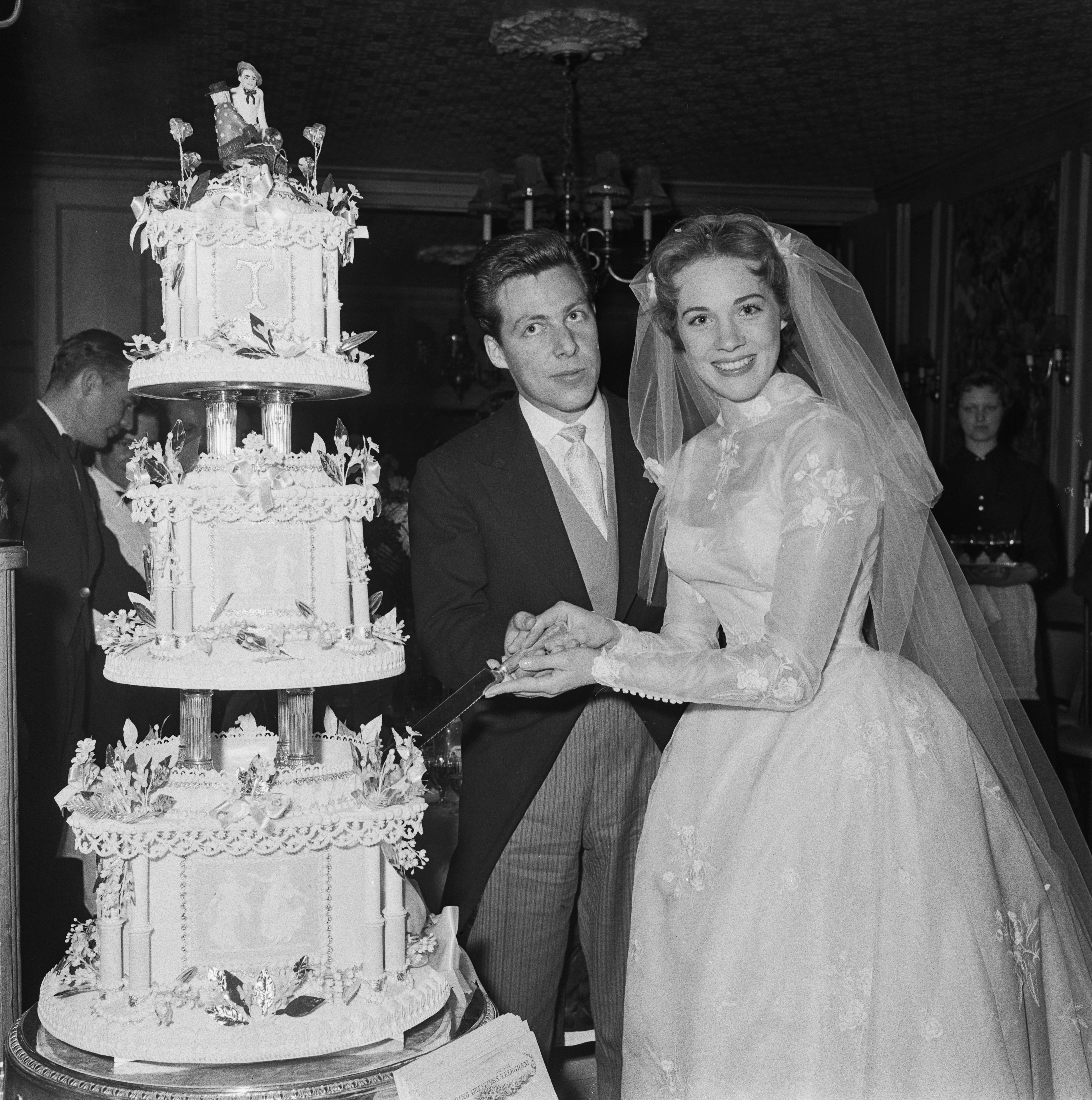 Bride and groom cutting a multi-tiered wedding cake with intricate decorations, both smiling and in formal wedding attire